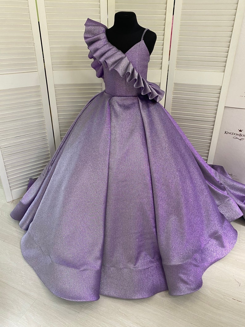 May include: A purple sparkly sleeveless dress with a ruffled one-shoulder neckline. The dress has a full skirt and is perfect for a special occasion.