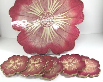 May include: A decorative floral serving tray and matching coasters. The tray and coasters feature a red and gold floral design. The tray is large and flower-shaped, with a gold rim. The coasters are also flower-shaped, with a similar design.