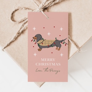 May include: A pink Christmas gift tag with a cartoon dachshund wearing a plaid scarf and Christmas lights. The text on the tag reads "Merry Christmas Love. The Paceys."