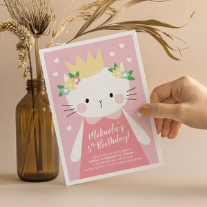 Może przedstawiać: R&oacute;żowe zaproszenie na urodziny z białym kotem w koronie i kwiatami. Tekst brzmi "Mikaela's 5th Birthday!" z informacjami o przyjęciu.