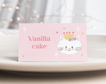 May include: A rectangular light pink card featuring the text Vanilla cake in a pink serif font. To the right, a white cat illustration wears a yellow crown with small flowers. The design includes scattered colorful dots and white starbursts.