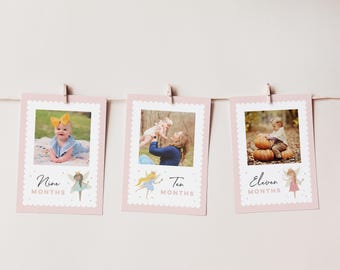 May include: Three pink photo cards with scalloped edges are hanging from a string. Each card has a photo of a baby and the words "Nine Months", "Ten Months", and "Eleven Months". Each card also has a fairy illustration.