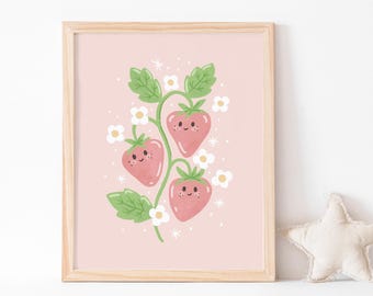 May include: A framed print featuring a whimsical illustration of three smiling strawberries on a vine with green leaves and white flowers. The background is a soft pink, and the frame is made of light-colored wood. The artwork has a cheerful, playful aesthetic.