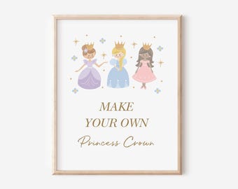 May include: A framed wall art print featuring three illustrated princesses wearing gold crowns, with the text "MAKE YOUR OWN Princess Crown" in gold lettering. The princesses are dressed in purple, blue, and pink gowns, surrounded by small stars and flowers.