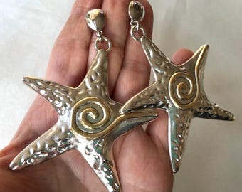 May include: A pair of silver and gold tone starfish earrings with a textured finish and a spiral design.
