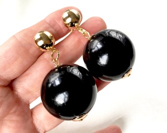 May include: A pair of dangle earrings with large black round beads and gold accents.
