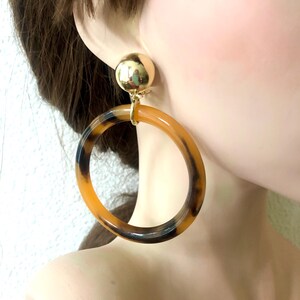 May include: A pair of large, round, brown and black hoop earrings with a gold clip-on closure.