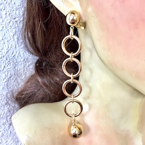 May include: Gold tone clip-on earrings with a dangling chain of four connected circles and a round ball at the end.