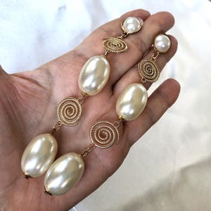May include: A pair of long drop earrings featuring gold-tone metal spiral links alternating with smooth, oval-shaped cream-colored faux pearls. Each earring terminates in a round faux pearl stud at the top, connected by gold-tone metal chains.