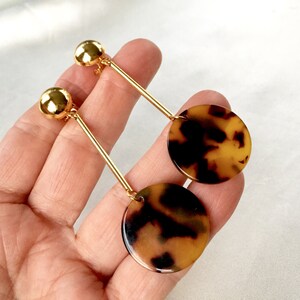 May include: Gold dangle earrings with a brown and black tortoiseshell pattern circle pendant.