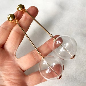 May include: Gold tone clip-on earrings with a long, thin gold bar and a clear glass sphere at the end.