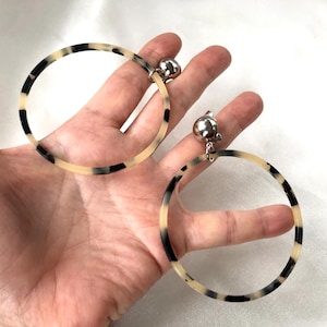 May include: A pair of large, round, tortoiseshell hoop earrings with silver clip-on closures.
