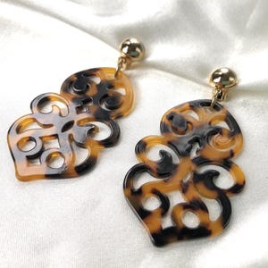 May include: A pair of brown and black tortoise shell clip-on earrings with a gold-tone metal clasp. The earrings are in the shape of a stylized floral design.