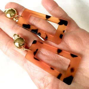 May include: A pair of large, rectangular earrings with a tortoiseshell pattern. The earrings have a gold-tone finish and are made of acrylic.