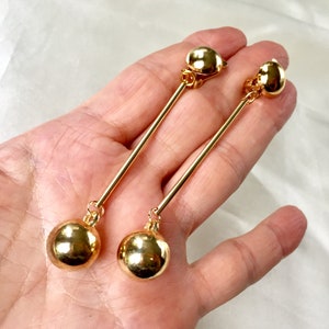 May include: A pair of gold clip-on earrings with long, thin, gold rods and large, round, gold balls at the bottom.