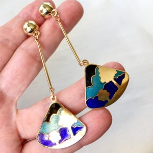 Könnte beinhalten: Ein Paar goldene Ohrhänger mit blauem, grünem, schwarzem und weißem Email. Die Ohrringe haben ein fächerförmiges Design mit einem stilisierten Baummotiv.