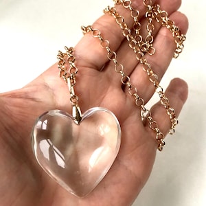 May include: A gold chain necklace with a large clear heart-shaped crystal pendant.