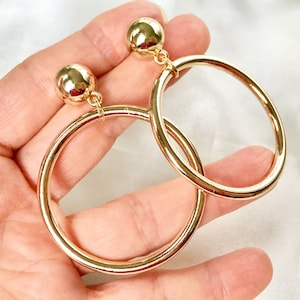 May include: A pair of gold hoop earrings with a large, round, gold ball dangling from each hoop.