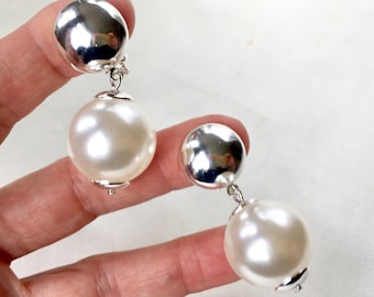 May include: A pair of silver and white pearl drop earrings. The earrings feature a large, round, white pearl dangling from a smaller, round, silver disc.