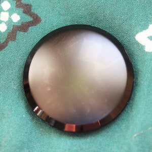 May include: A round, black, metal button with a smooth, shiny surface.