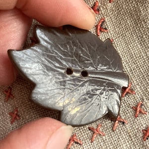Peut inclure: Un bouton en forme de feuille marron avec deux trous. Le bouton présente un motif de feuille détaillé et une surface légèrement texturée.