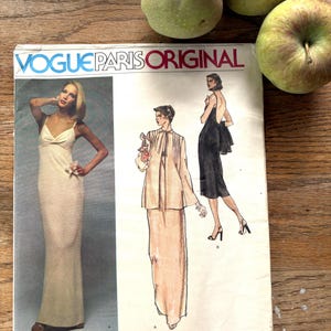 May include: A Vogue Paris Original sewing pattern envelope by Nina Ricci, number 1554. The front features a photograph of a floor-length white dress and illustrations of a two-piece outfit and a black dress with a low back design.