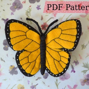 Puede incluir: Un patrón de mariposa de fieltro con contornos negros y puntos blancos. La mariposa es amarilla con marcas negras en las alas. El patrón está disponible para descargar en PDF.