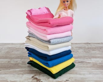 May include: A stack of folded blankets in various colors, including pink, gray, white, and blue. The blankets are neatly arranged, showcasing a range of hues. The top blanket is a vibrant pink with a satin trim. The blankets are stacked on a wooden surface.