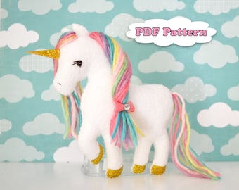 May include: A white plush unicorn with a rainbow mane and tail. The unicorn has a gold horn and a pink bow on its mane. The background is a blue and white cloud pattern. The text "PDF Pattern" is in a pink cloud shape.