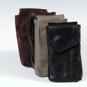 May include: Four leather phone cases in different colors: burgundy, dark green, gray, and black. The cases have a flap closure and a stitched design.
