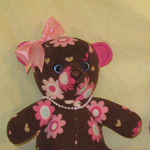 May include: Two plush teddy bears. One is brown with pink and white floral patterns, the other is pink with brown monkey patterns. Both have pink bows, pearl necklaces, and the name "Elise Anne" on their feet.