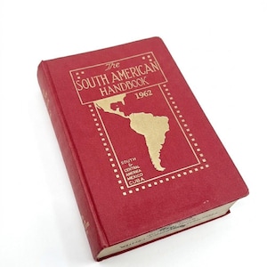 Puede incluir: Un libro rojo vintage titulado "The South American Handbook 1962". La portada presenta una ilustración dorada de Sudamérica y el texto "South & Central America Mexico Cuba."