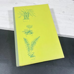 May include: A vintage book with a bright yellow cover featuring green illustrations of potted plants. The cover art includes a plant with long, pointed leaves, a flowering plant, and a fern. The book's spine is a muted green.