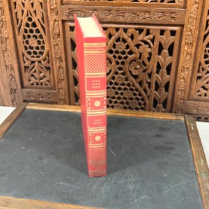 May include: A red hardcover book titled "Marie Antoinette" by Joan Haslip. The spine features gold decorative patterns and text. The book is set against a dark background with a wooden carved screen.