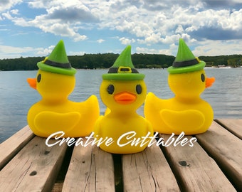 May include: Three yellow rubber duckies wearing green witch hats with black bands. The ducks are sitting on a wooden dock overlooking a lake.