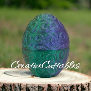 May include: A decorative egg with a green and purple swirling pattern. The egg is sitting on a tree stump. The text "Creative Cuttables" is visible below the egg.