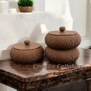 May include: Two brown ceramic containers with lids. The containers have a geometric diamond pattern and are stacked on top of each other. The containers are on a brown marble surface.