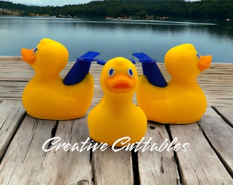 May include: Three yellow rubber duck toys with blue wings, sitting on a wooden surface. The ducks are facing forward, with the middle duck looking directly at the camera.
