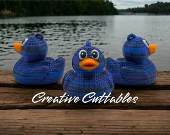 May include: Three blue and black striped rubber duck toys with orange beaks and white eyes are sitting on a wooden dock. The ducks are facing different directions. The text "Creative Cuttables" is written on the dock in white.