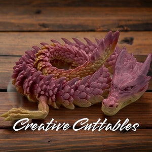 May include: A curled up pink and yellow dragon cake mold. The dragon has a detailed head and scales.