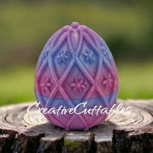 May include: A pink and blue decorative egg with a diamond pattern and floral accents. The egg is sitting on a wooden stump.  CreativeCuttables.