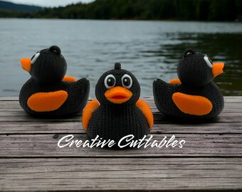 May include: Three black knitted rubber duck toys with orange beaks and feet. The ducks are sitting on a wooden surface. The ducks are facing different directions. The text "Creative Cuttables" is visible in the bottom center of the image.