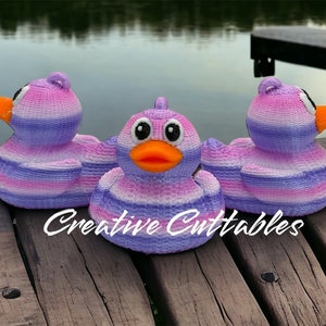 May include: Three purple and pink striped rubber duck toys with black eyes and orange beaks. The ducks are sitting on a wooden surface. The text "Creative Cuttables" is visible in the bottom center of the image.