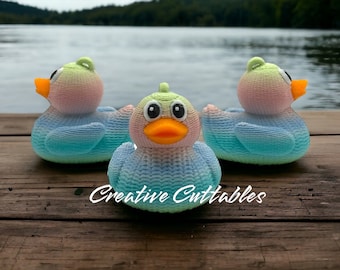 May include: Three rubber duck toys with a gradient of blue, green, and pink colors. The ducks are sitting on a wooden surface. The text "Creative Cuttables" is visible in the image.
