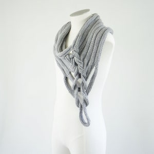 Puede incluir: Una bufanda de punto gris con un diseño trenzado único. La bufanda se muestra en un maniquí blanco.