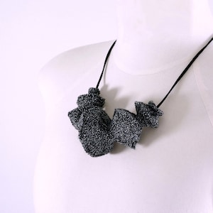 May include: A black and silver knit necklace with a geometric design. The necklace is made of multiple pieces of knit fabric that are connected together.