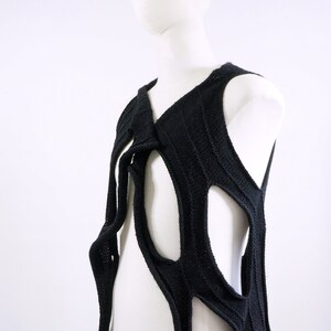 May include: A black knitted sleeveless top with a unique, abstract design featuring large cutouts. The top is made of a soft, textured knit fabric.