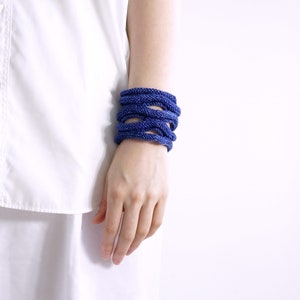 Könnte beinhalten: Nahaufnahme eines Handgelenks, das einen Stapel blauer gewebter Armbänder trägt. Die Armbänder bestehen aus einem dicken, strukturierten Material und sind übereinander gestapelt.