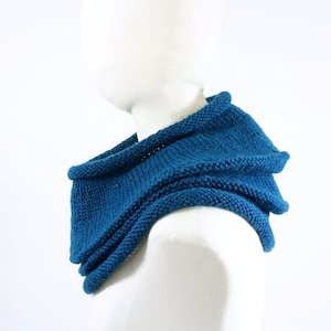 Könnte beinhalten: Ein türkisfarbener gestrickter Schal mit Rollkragen und gefaltetem Design. Der Schal ist über eine weiße Schaufensterpuppe gelegt.