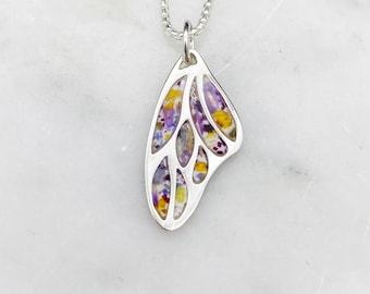 May include: A silver chain necklace with a delicate butterfly pendant. The butterfly wings are made of clear resin with embedded dried flowers in shades of purple, yellow, and white.